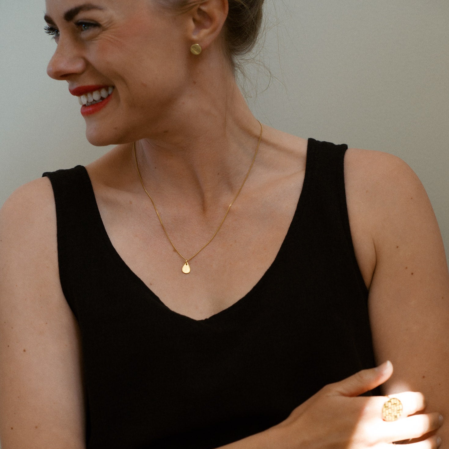 Woman wearing PS46 Jewelry Tears of Hope Pendant Necklace, earrings and a ring, smiling while wearing a black sleeveless top.