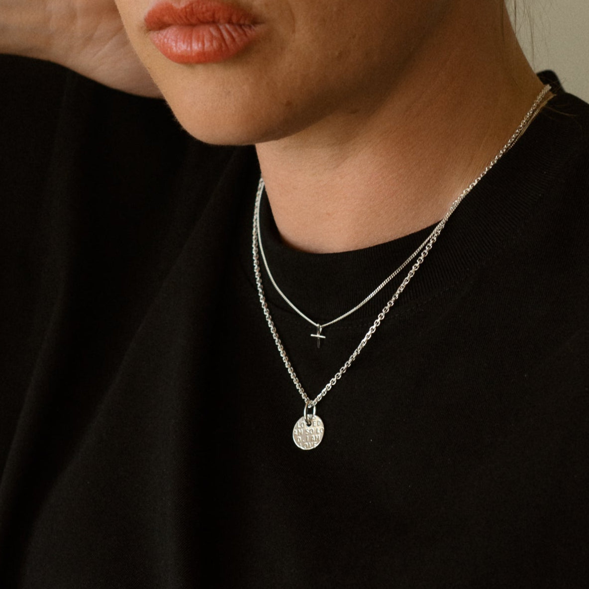 Woman wearing a black top and layered necklaces against a neutral background