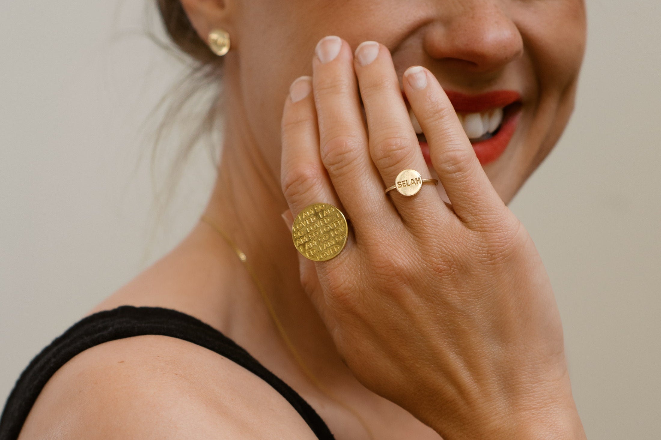 Woman wearing gold jewelry including a ring and necklace, with a neutral background.