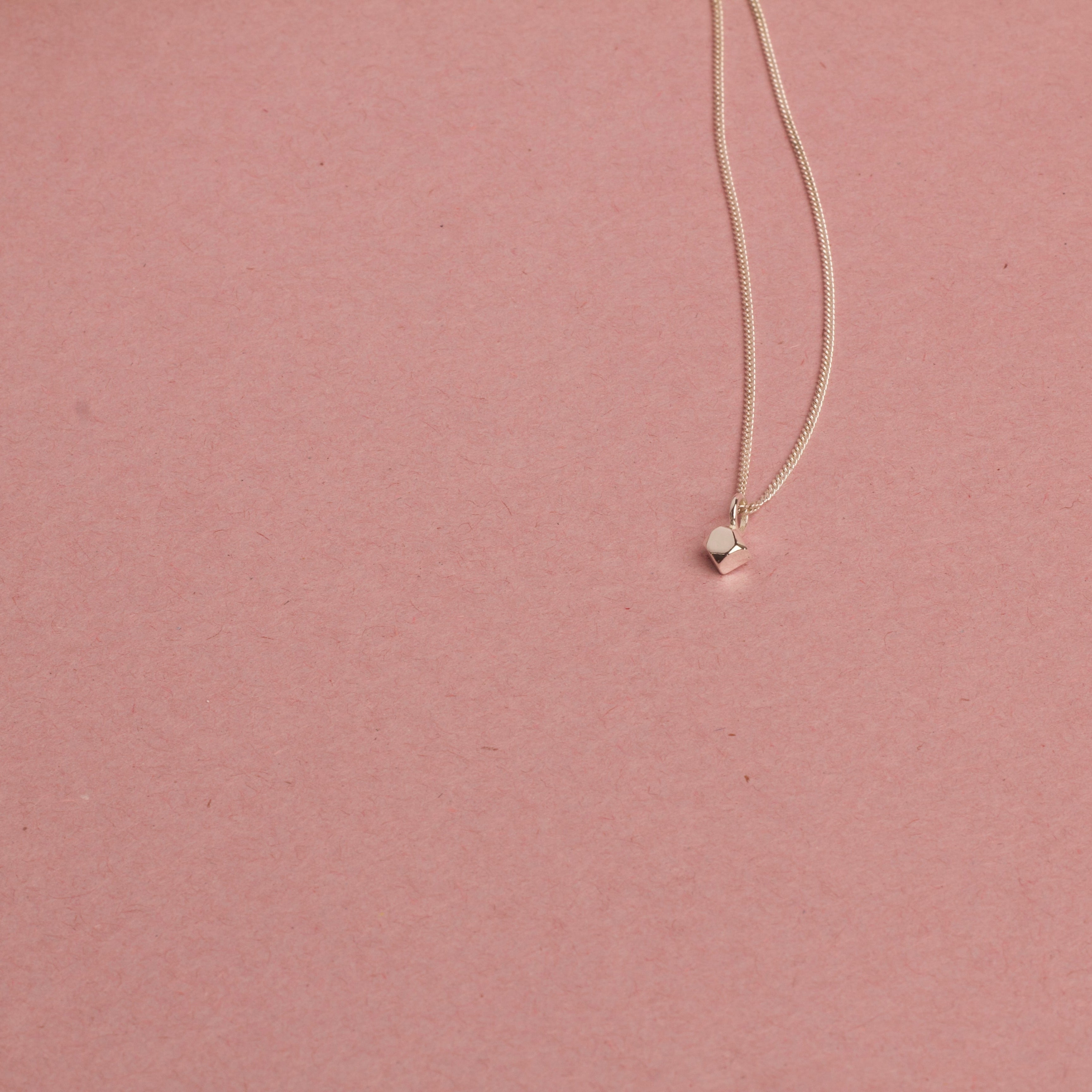 Necklace with a small white gold pendant on a pink background