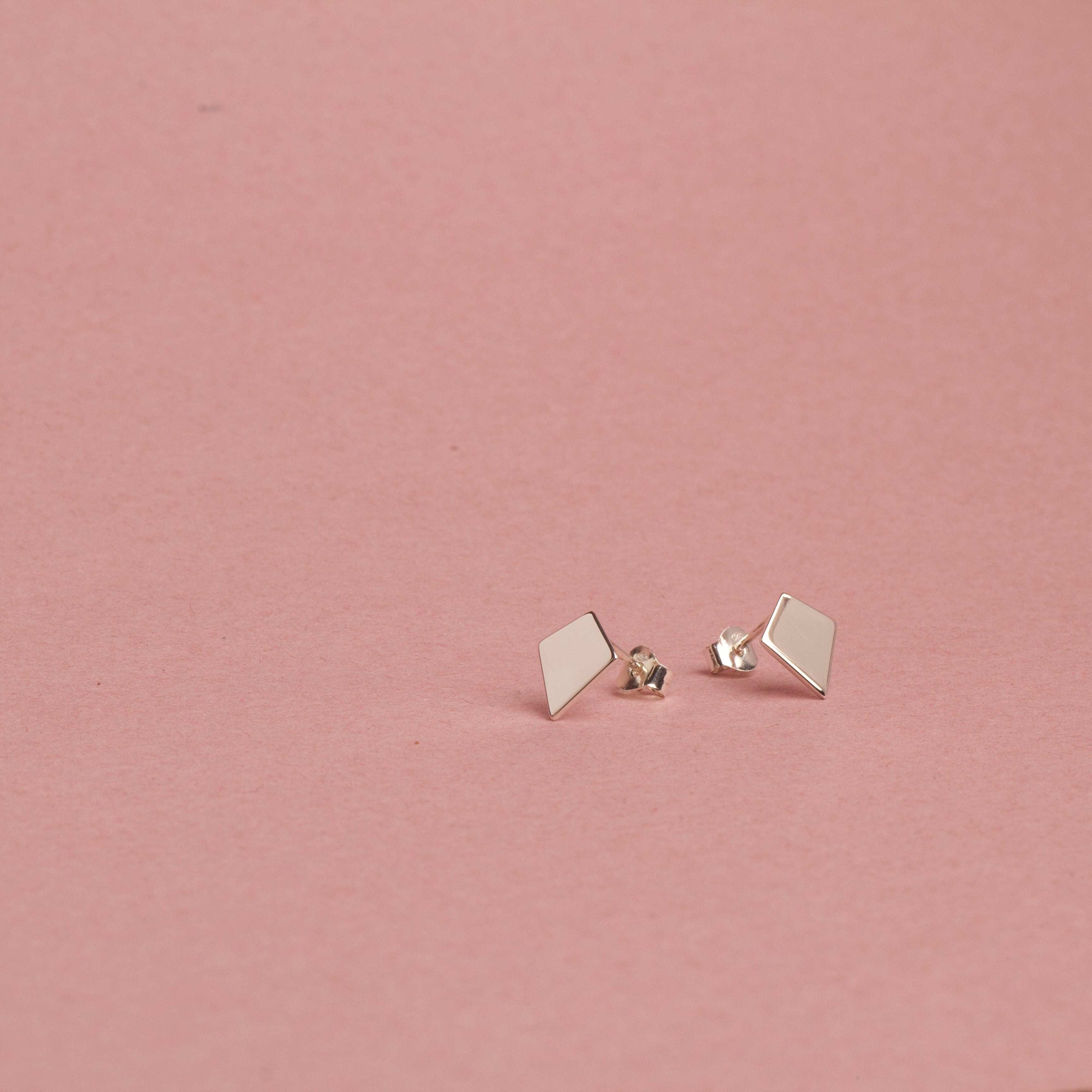 Pair of 18K white gold geometric earrings on a pink background, shield of faith, stud