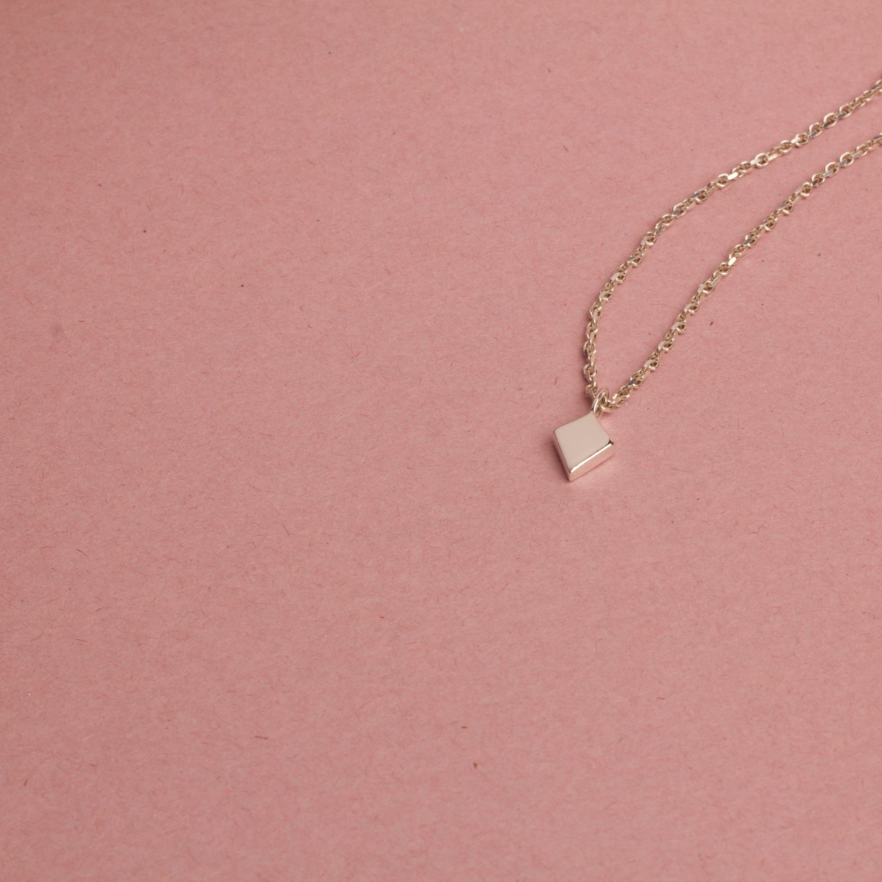 White gold necklace with a square pendant on a pink background, shield of faith