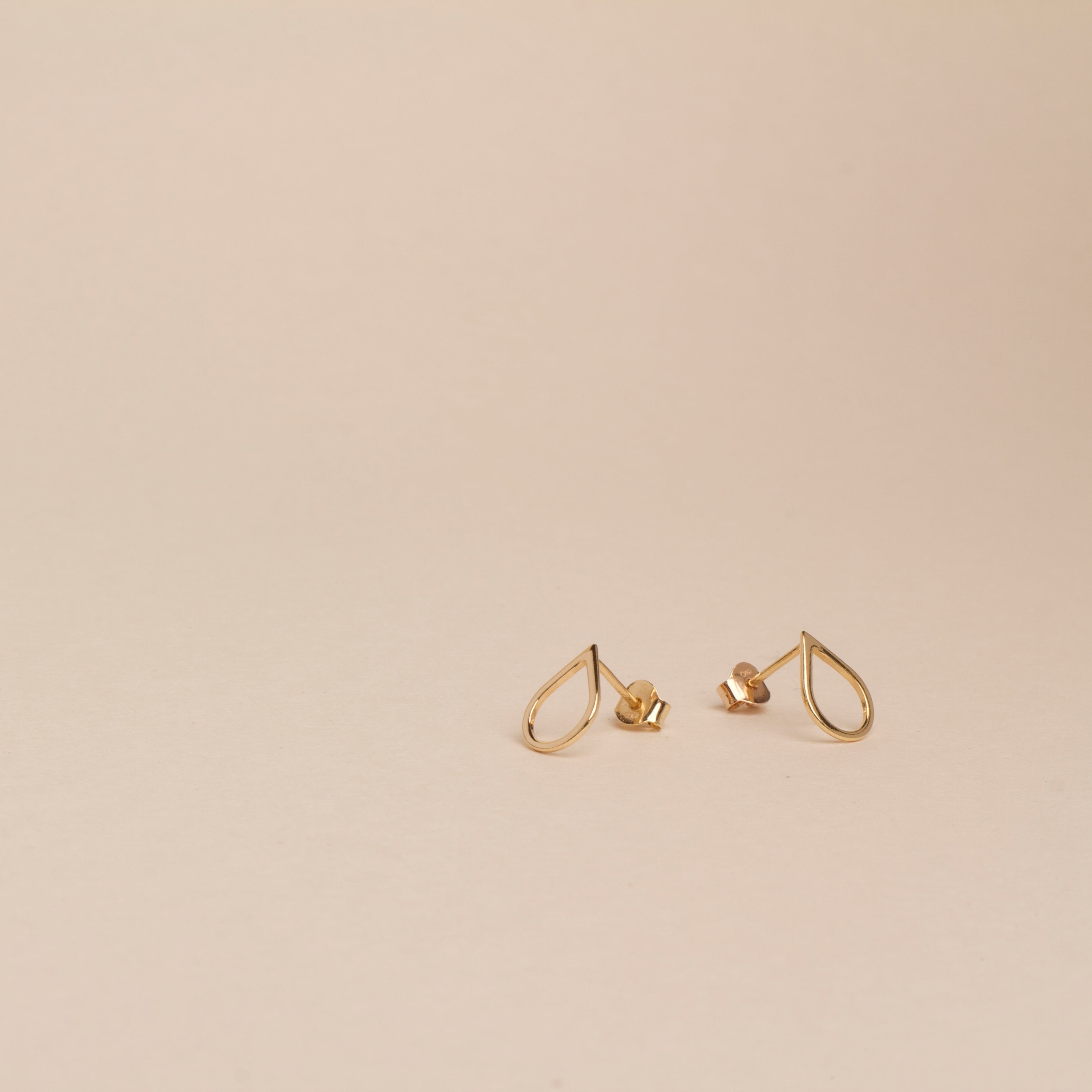 Pair of gold earrings on a beige background, tears of hope