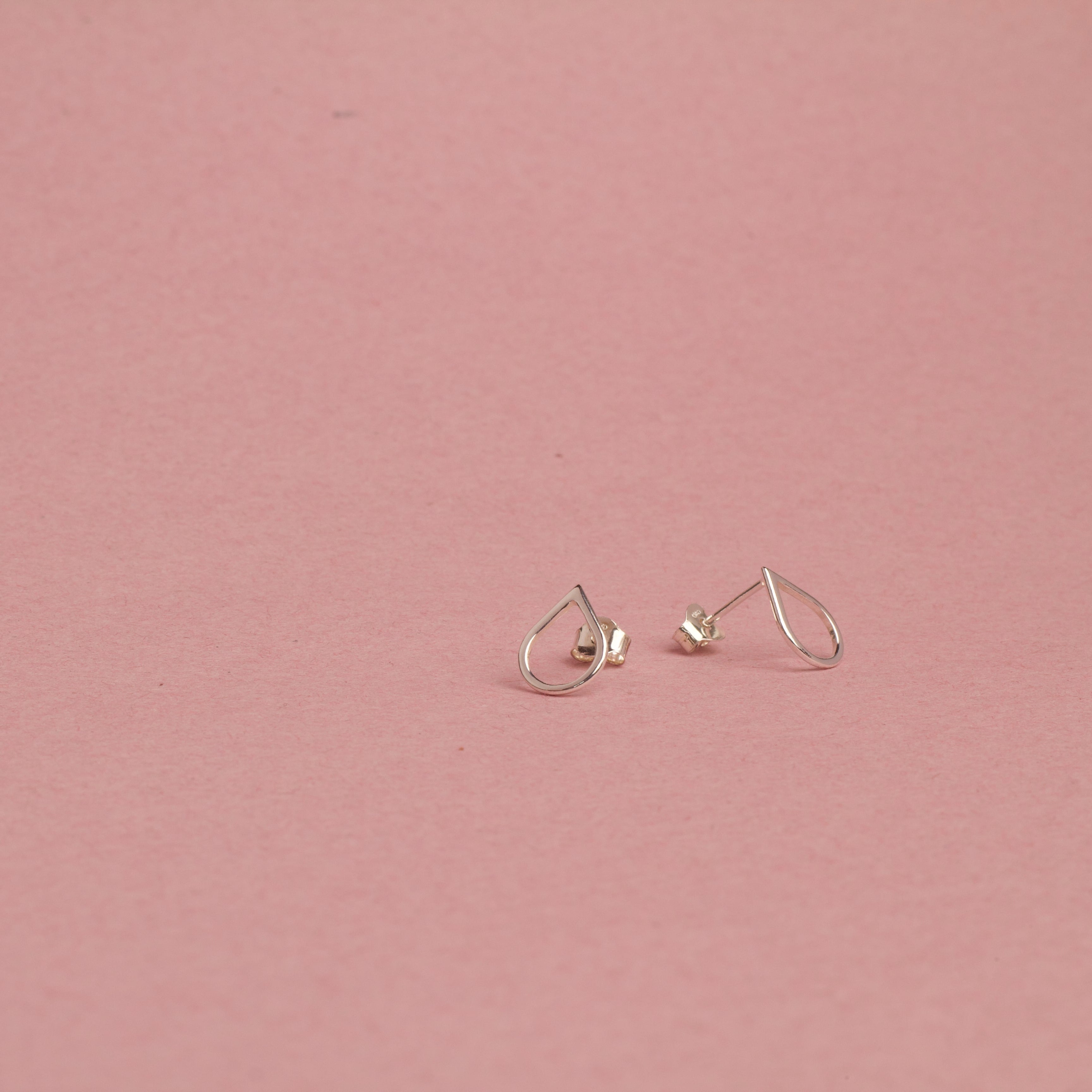 Pair of white gold earrings on a pink background, tears of hope