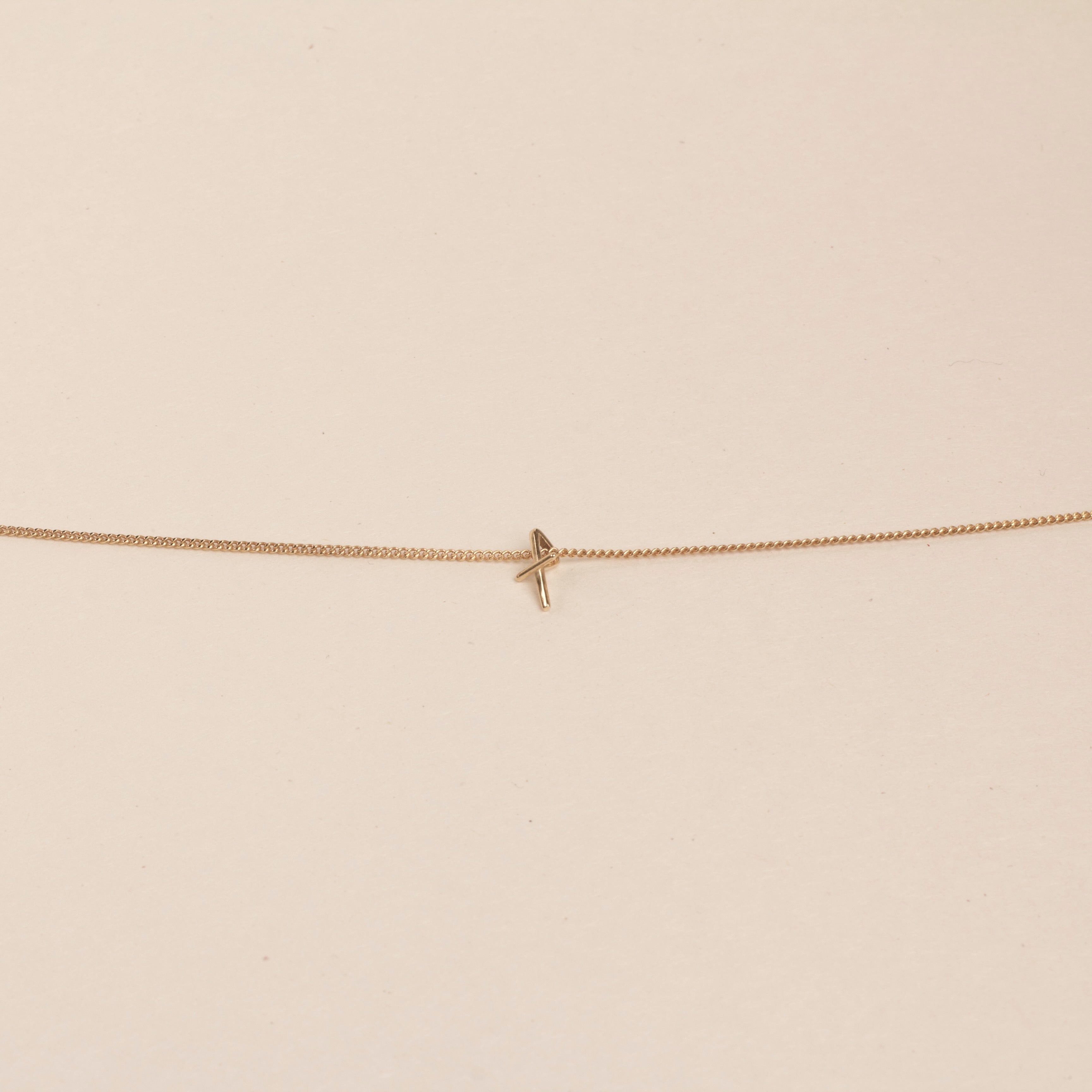 18K Gold necklace with a small cross pendant on a beige background