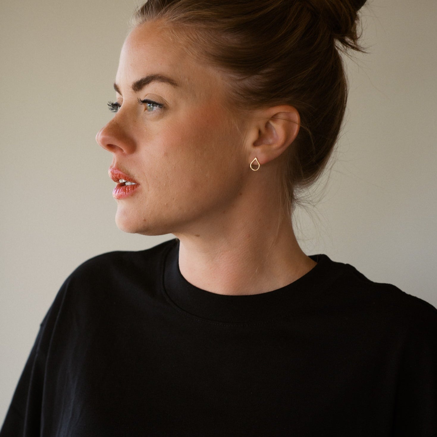 Woman wearing a black top against a neutral background, white gold earrings, tears of hope.