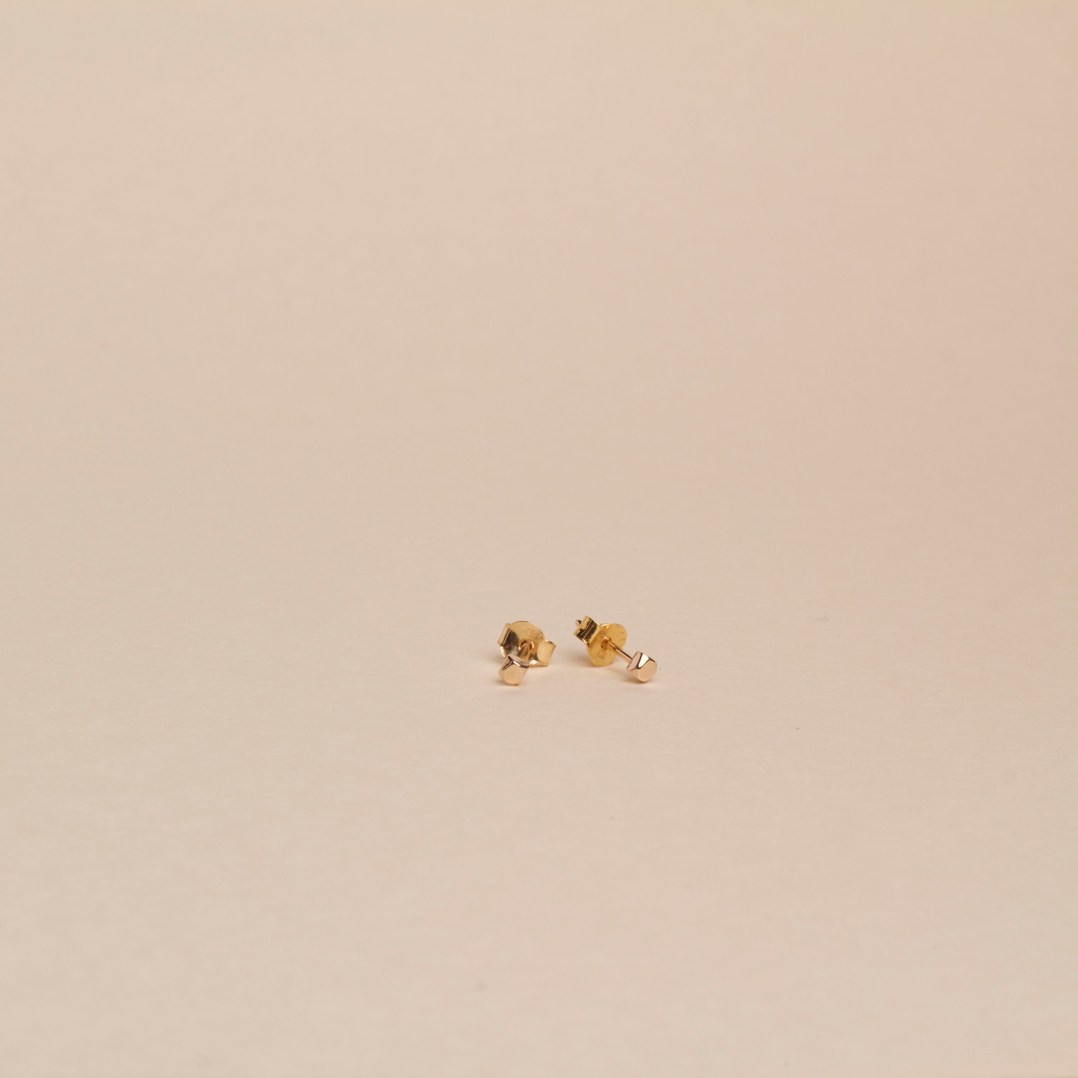 Pair of Righteousness small 18K gold earrings on a beige background.