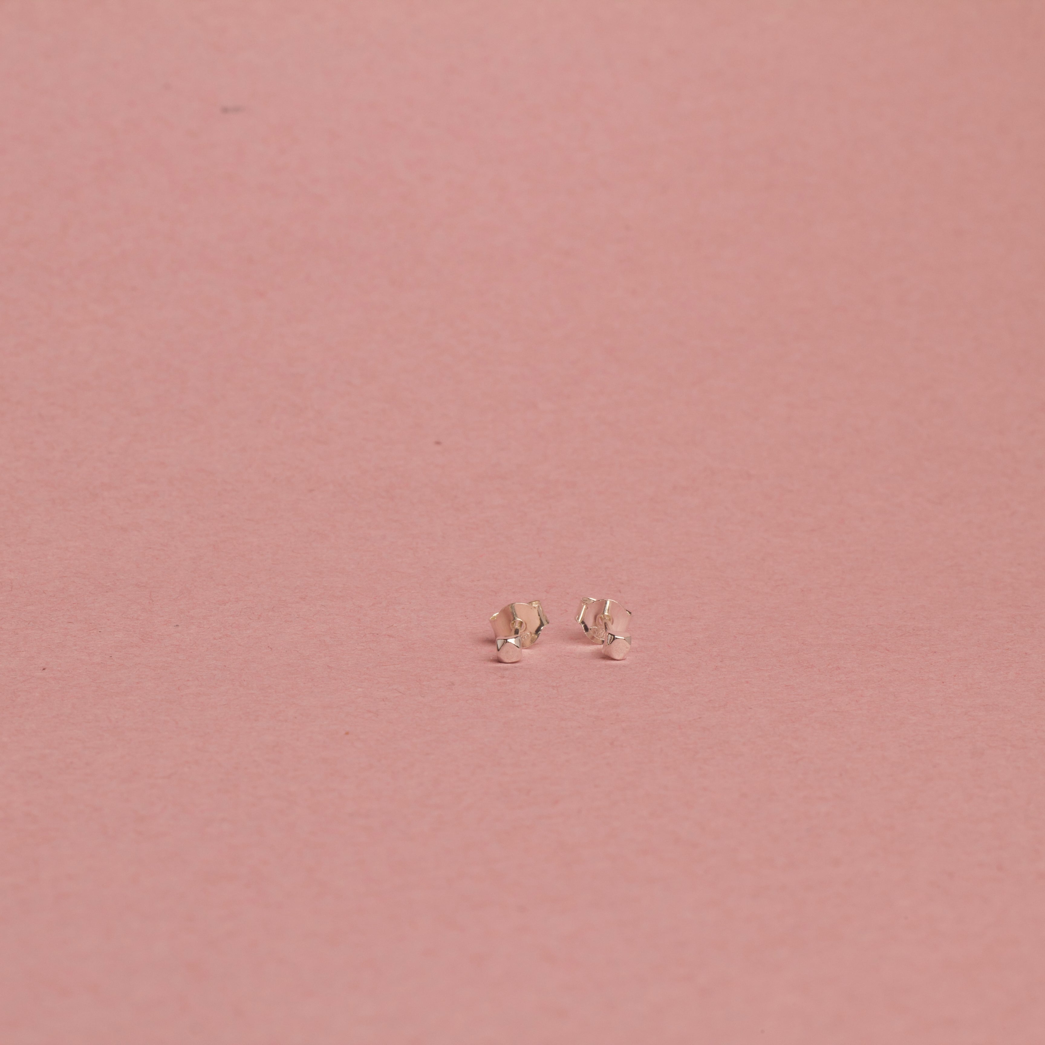 Pair of Righteousness small white gold earrings on a pink background.