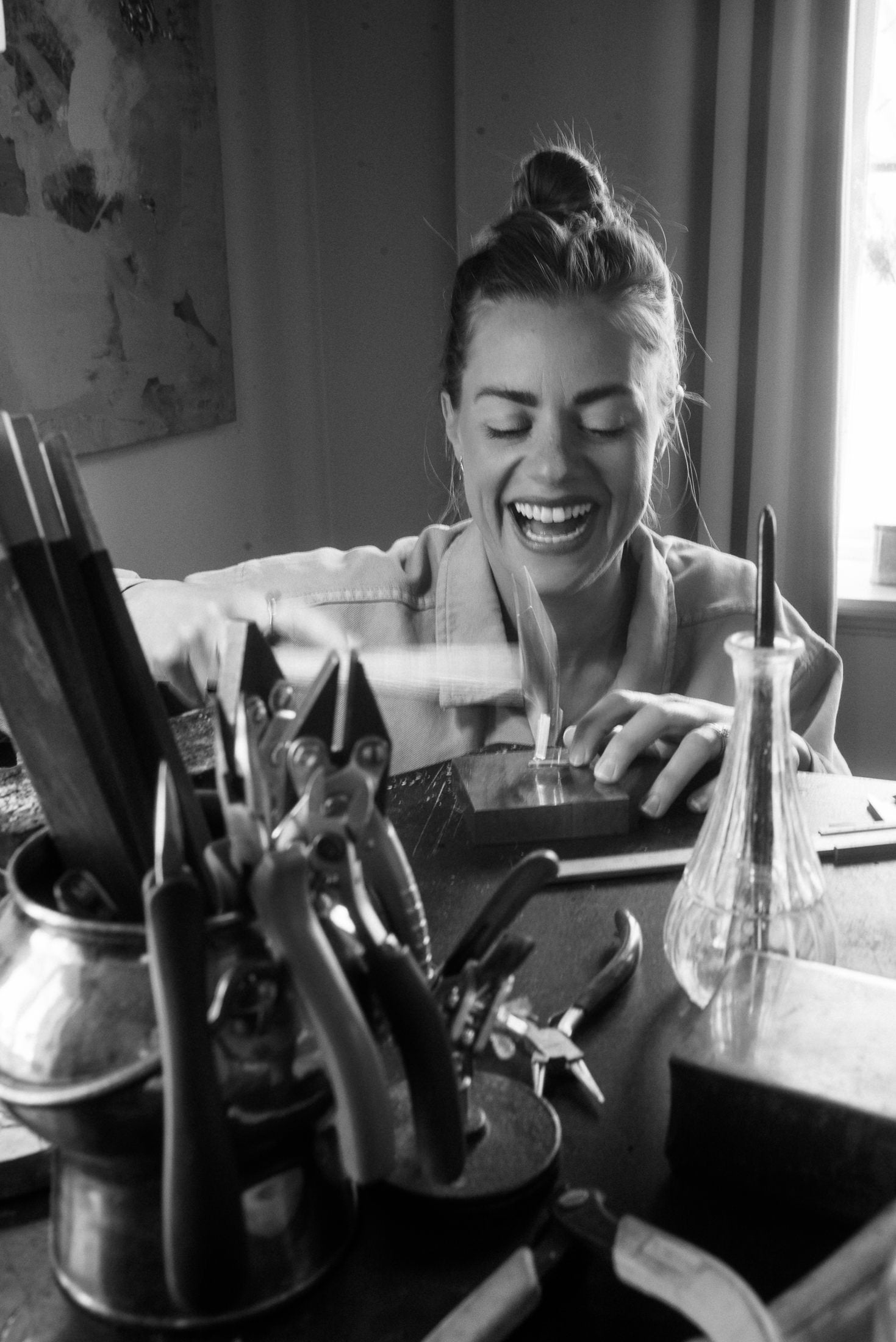 Person sitting at a desk with various items around, laughing. Emelie the jewelry designer
