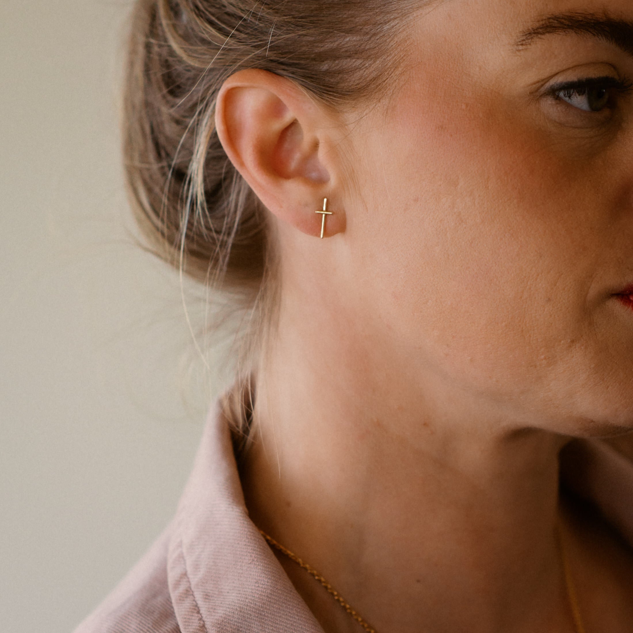 Close-up of a person wearing a 18K gold cross earring with a neutral background