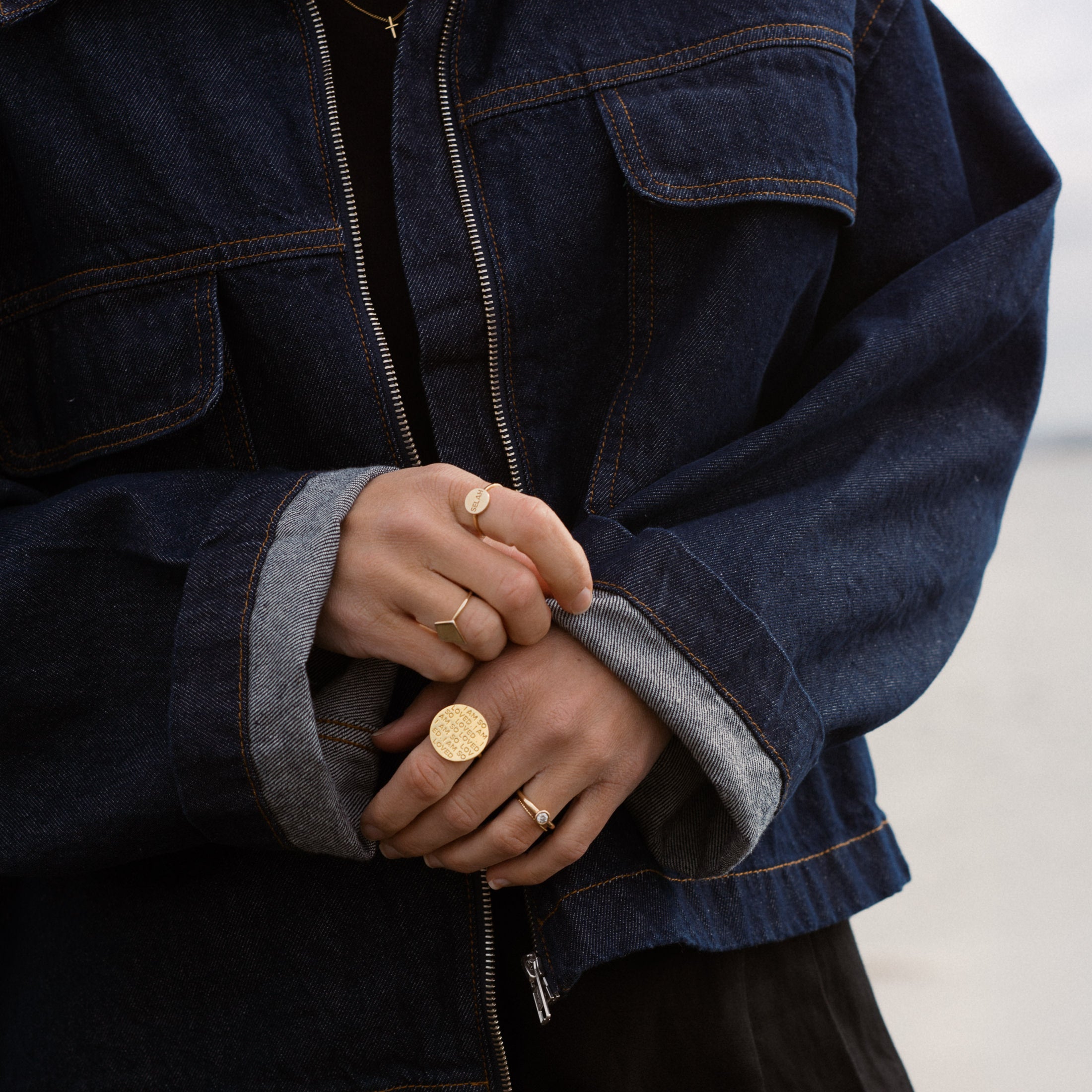 Person wearing a blue denim jacket with gold rings on fingers