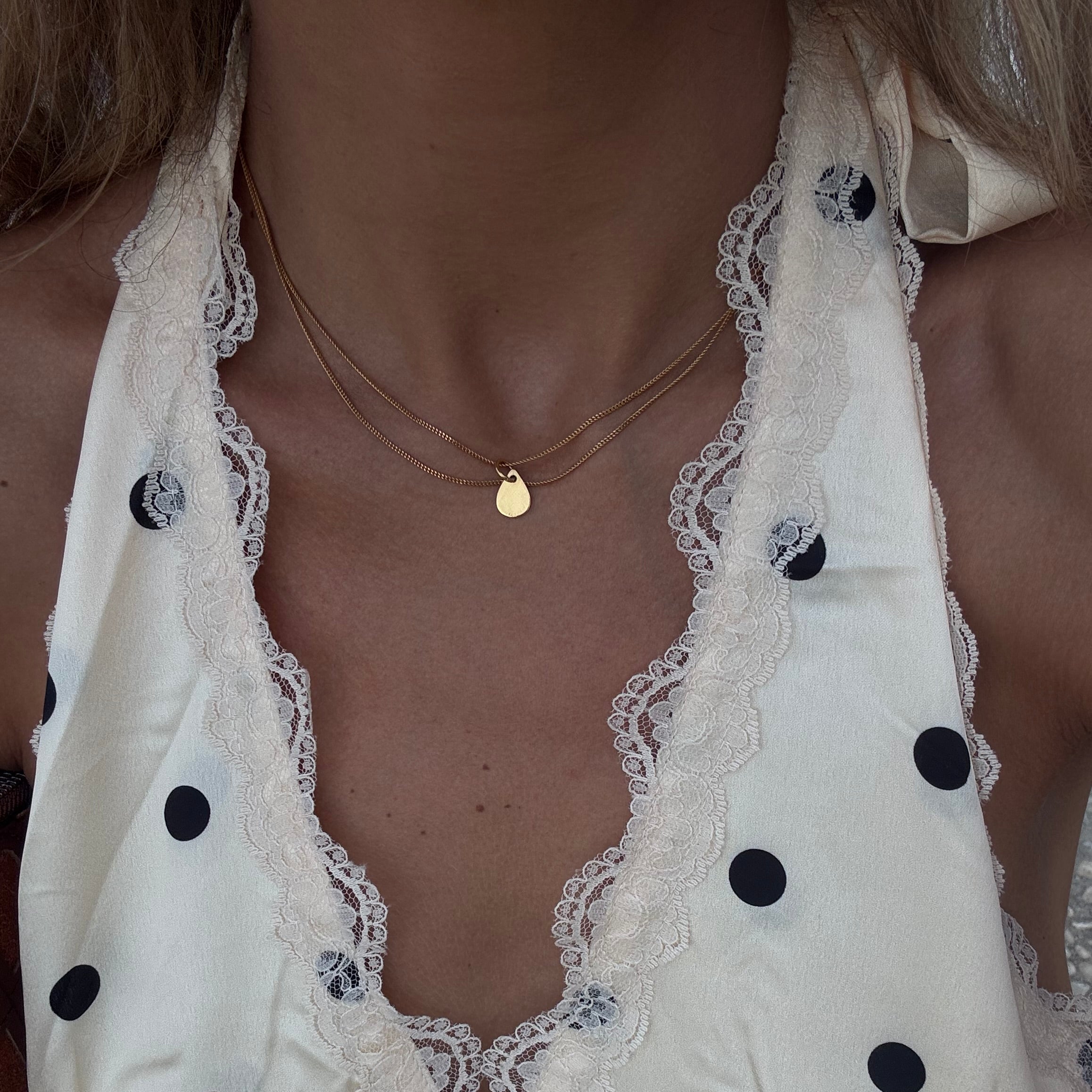 Woman wearing a white polka dot dress with lace trim and PS46 Jewelry Tears of Hope Pendant Necklace layered with another chain.