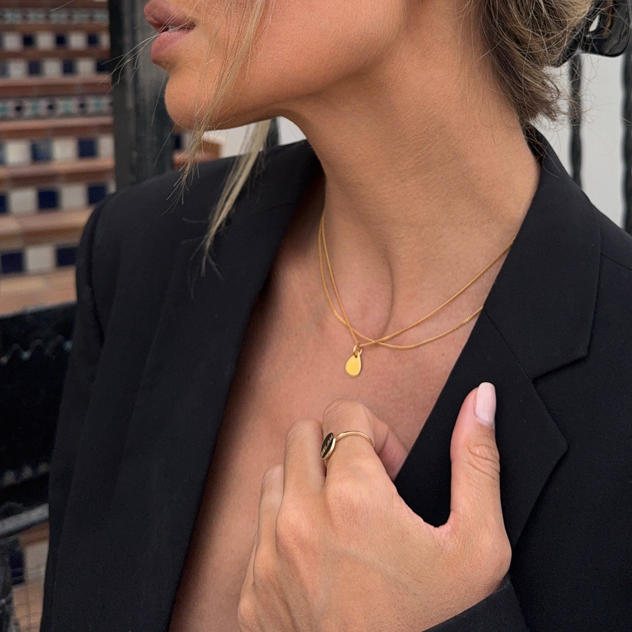 Woman wearing PS46 Jewelry Tears of Hope Pendant Necklace 18K Gold layered with another chain, wearing a ring and a black blazer.