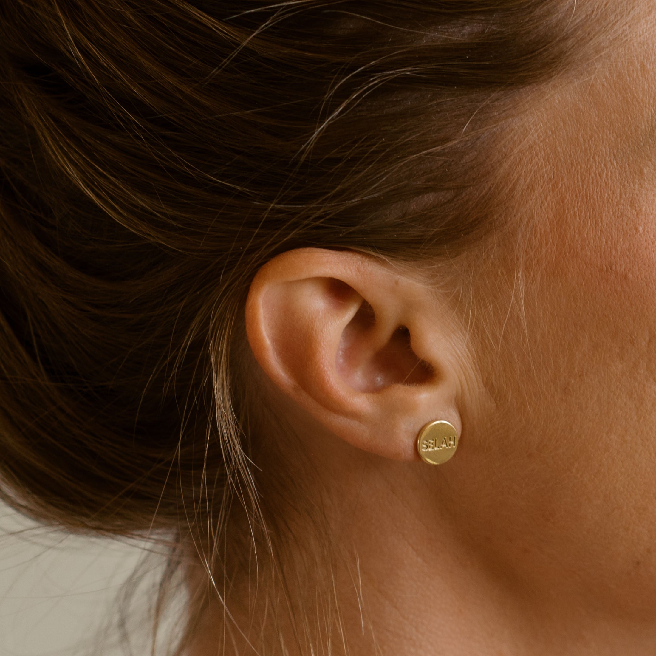 Gold earring worn by a person with brown hair.