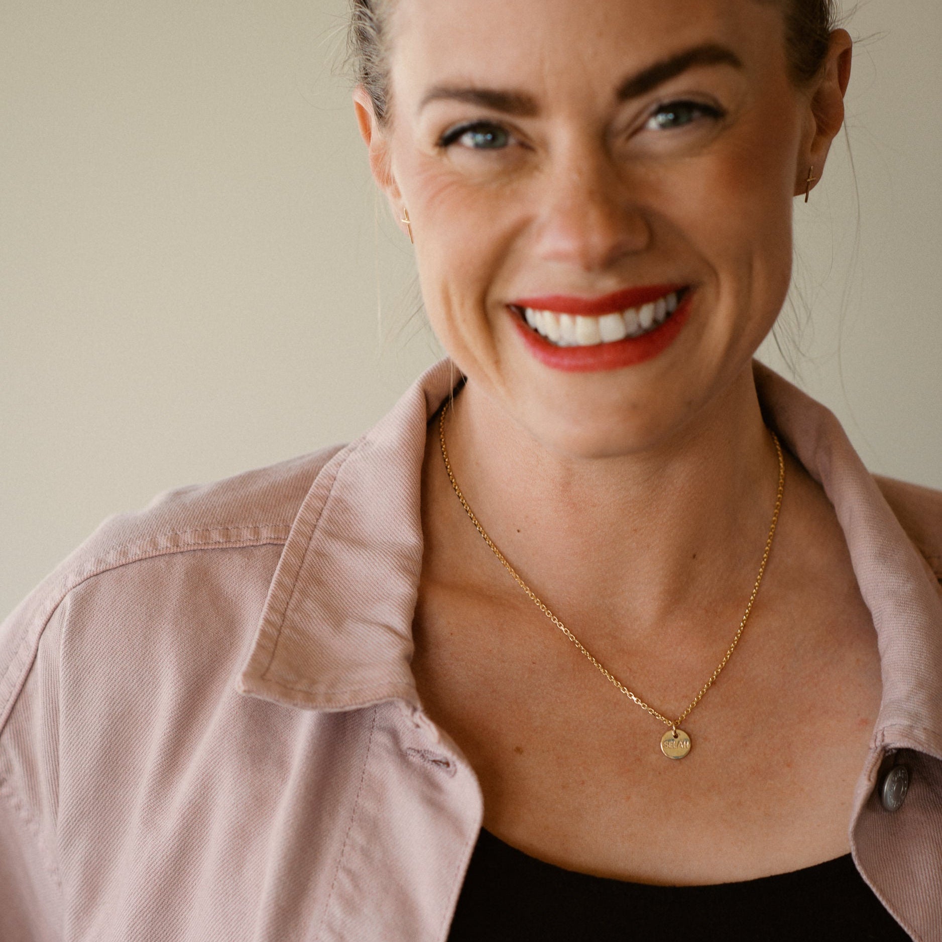 Woman wearing a pink shirt and gold necklace with a plain background