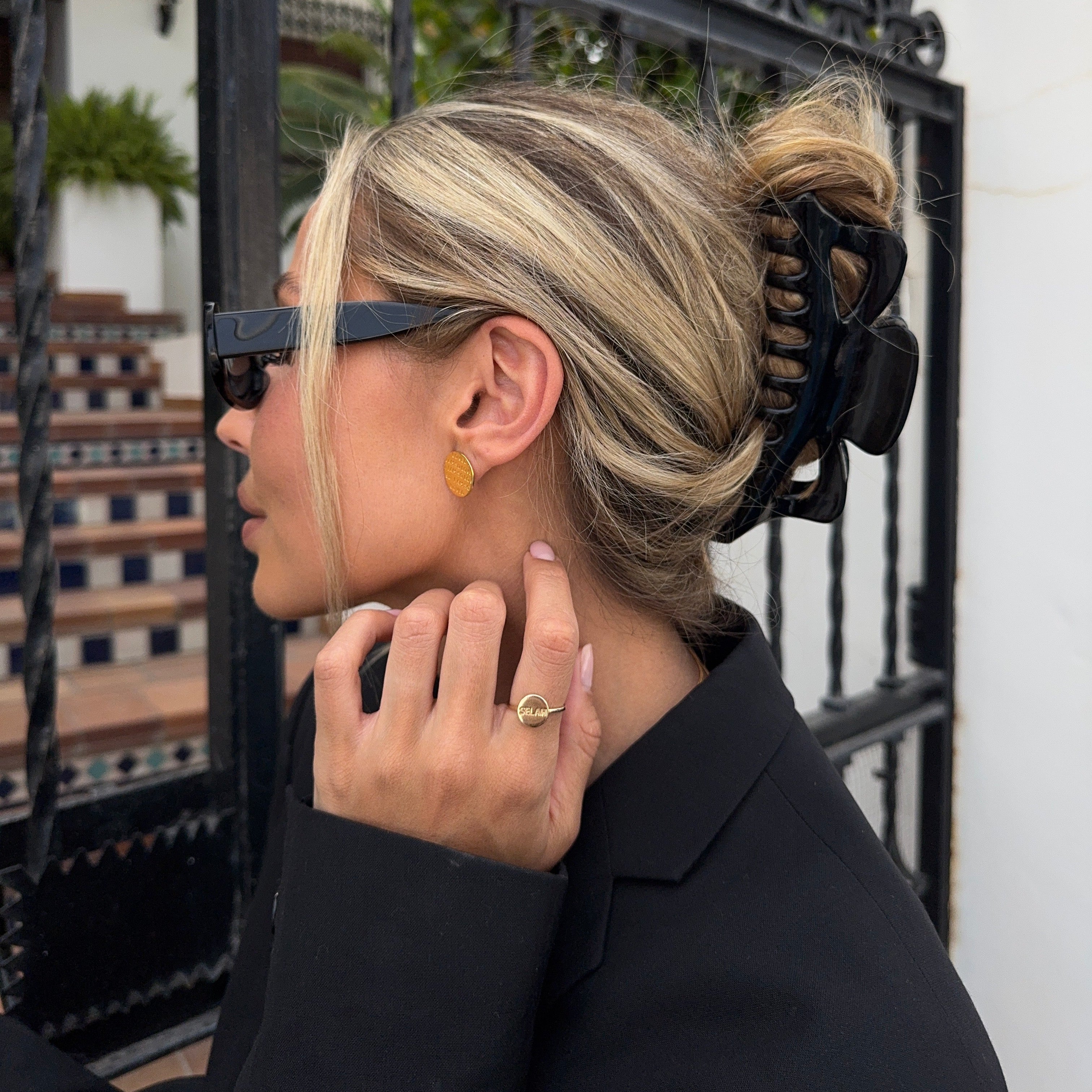 Person with blonde hair styled in a bun, wearing a black top, standing near a black metal gate.