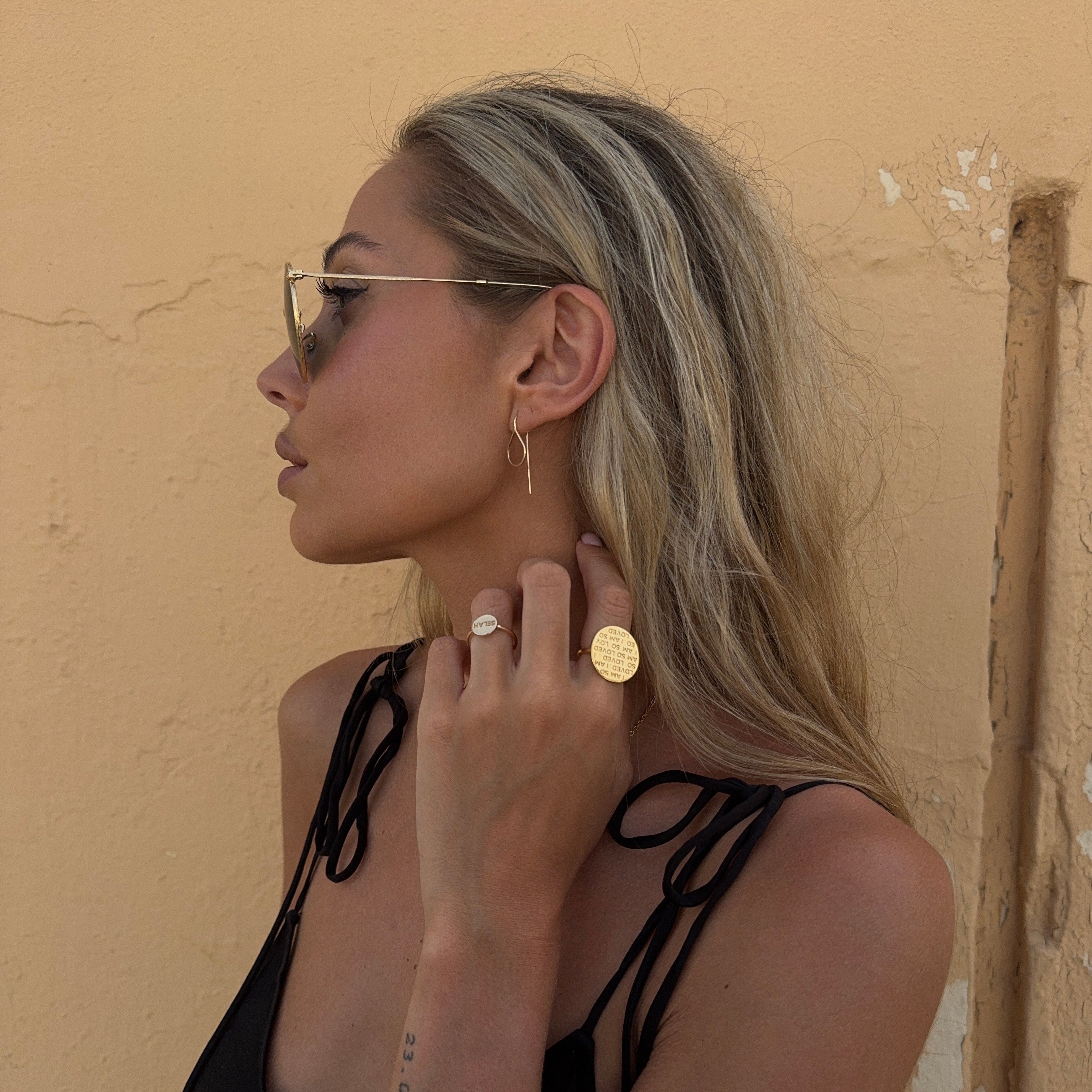 Woman adjusting a gold earring against a beige wall