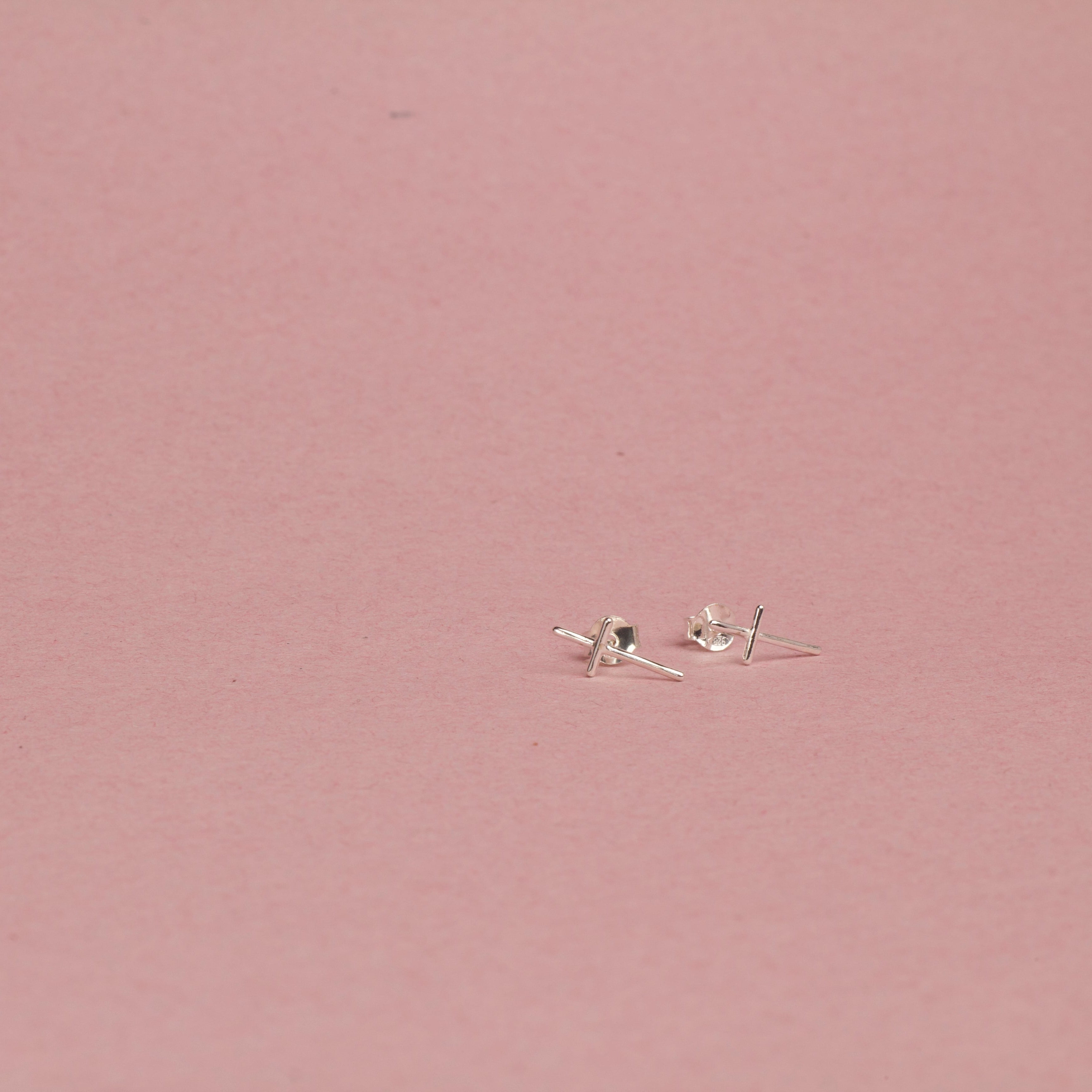 Small white gold cross earrings on a pink background