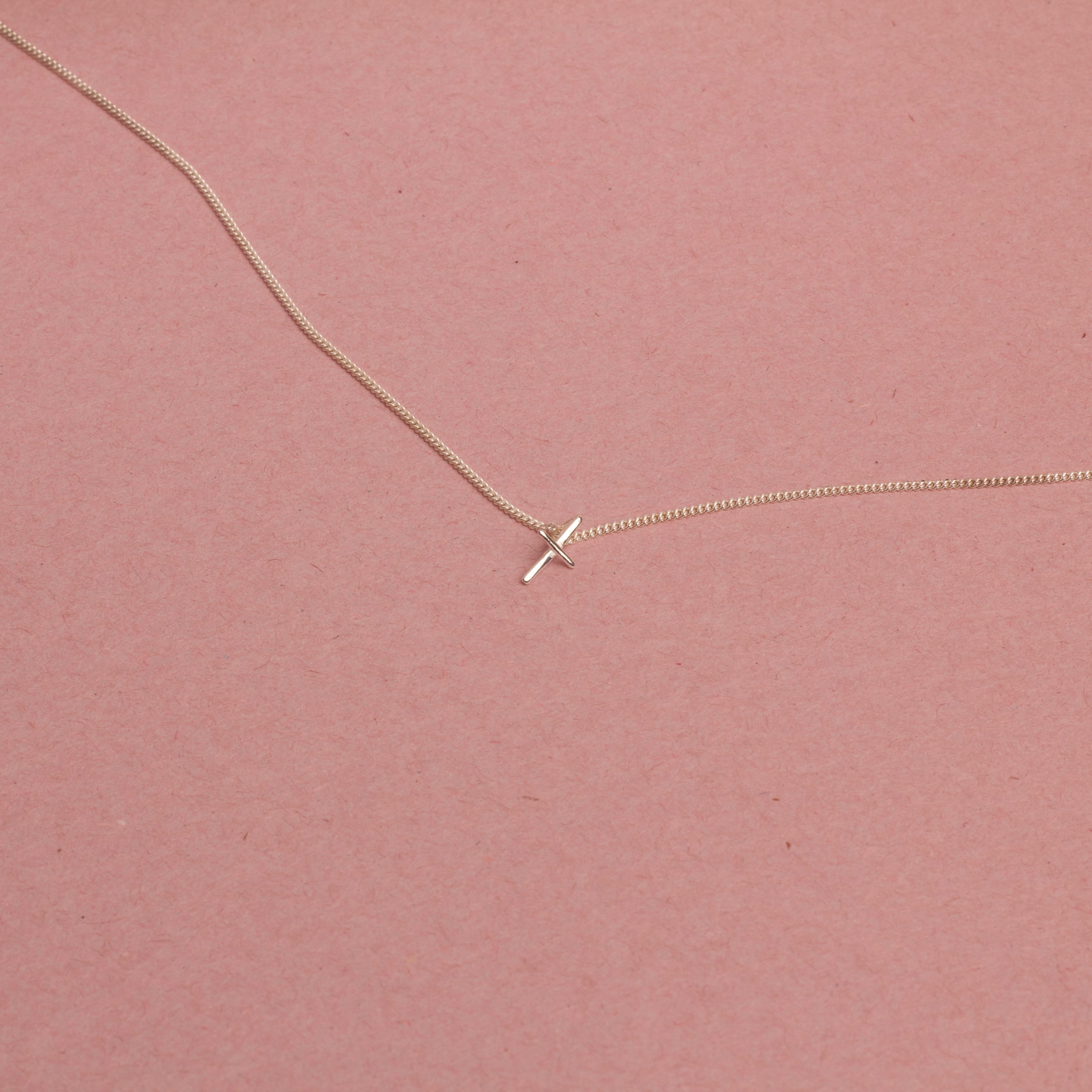 18K White gold necklace with a small cross pendant on a pink background