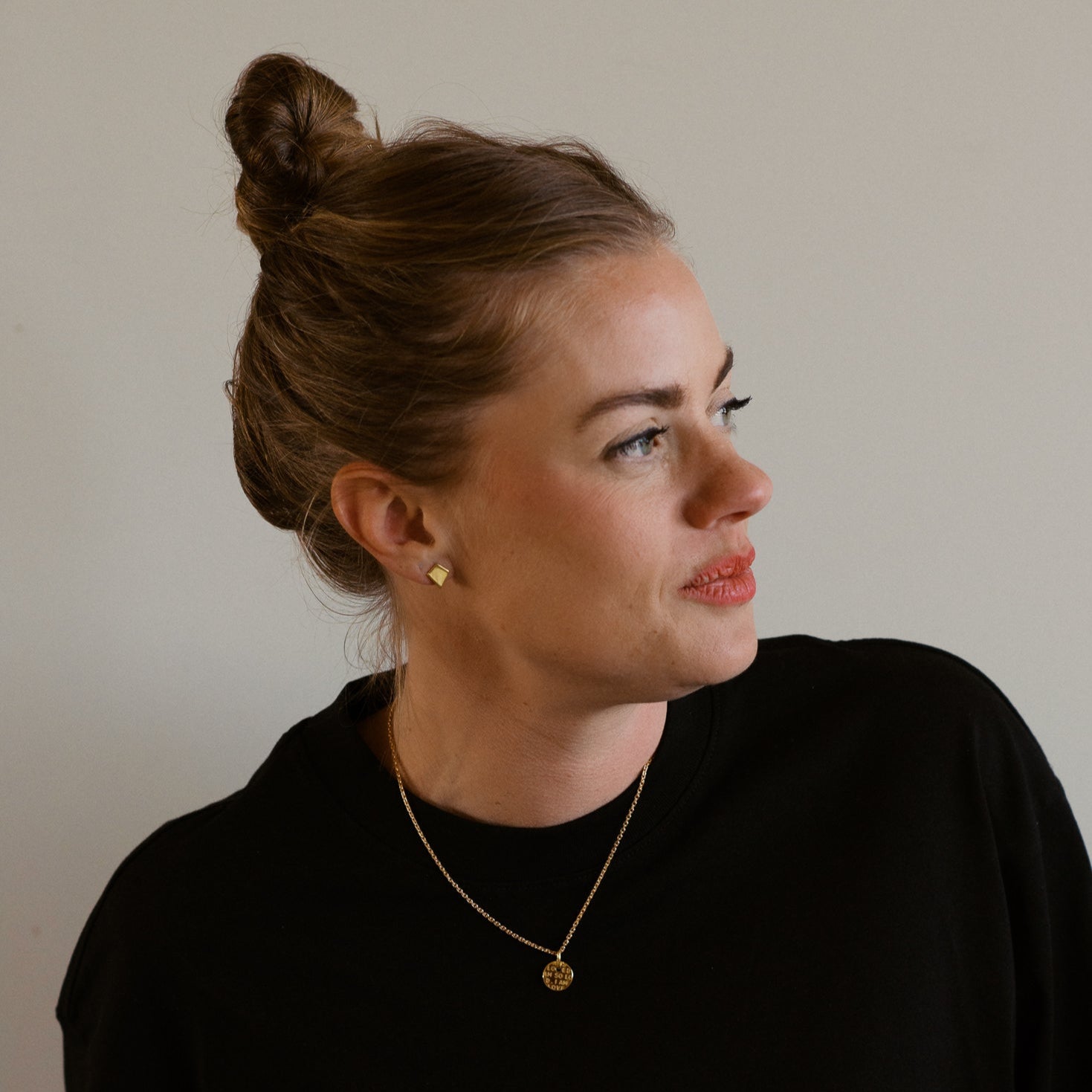 Woman wearing a black top and gold necklace against a plain background, 18K gold, shield of faith, stud