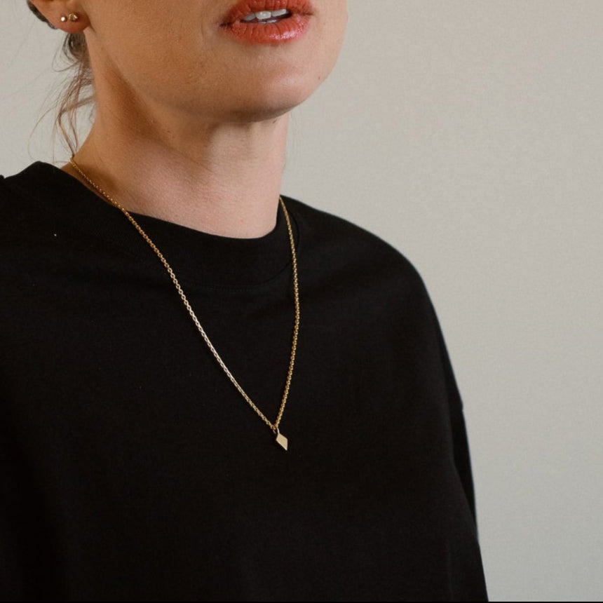 Woman wearing a black sweater against a plain background, 18K gold necklace, shield of faith